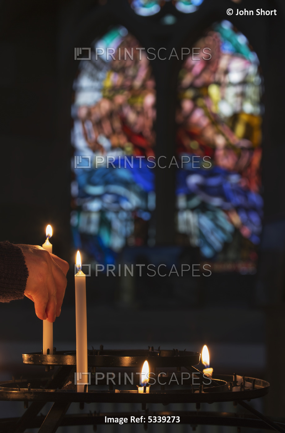 A Man's Hand Lights A Candle In A Church With Colourful Stained Glass Window In ...