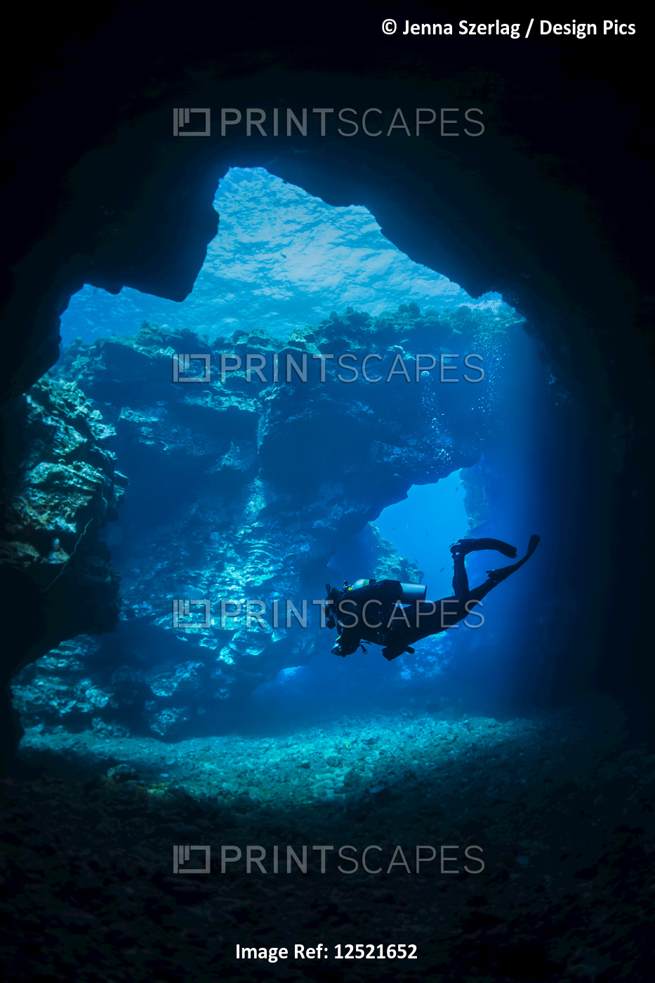 Scuba diver swims through lava arches with sun rays, Cathedrals dive site; ...